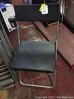 Single black folding chair with silver metal frame and black plastic seat and backrest, showing some surface wear and dirt on seat.