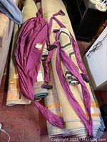 Photo showing the purple aerial yoga hammock and two sets of purple straps with black handles laid on rolled carpets on the floor.
