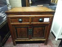 Full front view of the wooden Asian style cabinet side table showing two drawers on top and two decorated cabinet doors below.