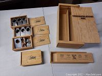 Multiple small Atlas branded wooden boxes containing metal wine tags and keychain accessories, displayed with their lids removed.