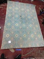 Full view of large rectangular area rug with blue and yellow floral diamond pattern on a red floor surface.