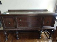 Front view of dark wooden dining buffet cabinet with drawers and doors, showing carved legs and details.