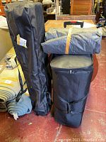 Photo showing three carrying bags: one tall and slim, one rolling bag with handle, and a folded gray cover on top of the rolling bag.