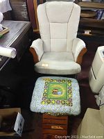 Front view of glider chair with removable beige cushioned cover and wooden arms, wooden ottoman with colorful padded cover featuring owls in front of the chair.