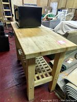 Side angle of the natural wood kitchen island with butcher block top and Toshiba microwave on top, showing the slatted lower shelf and sturdy wooden legs.