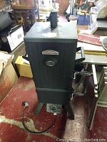 Full view of black vertical smoker with handle and power cord on a red floor.