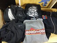 Photo showing folded black and grey Nike hoodies with swoosh logos and two hoodies with Hood to Coast Relay graphics.