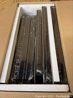 A box of multiple black rectangular art frames still wrapped in plastic packaging.