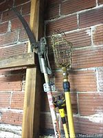 Photo showing Fiskars tree trimmer, fruit picking basket and lightbulb changer on extender poles leaning against a wooden frame and brick wall
