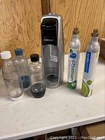 Front view showing SodaStream machine, three bottles, and three empty CO2 canisters on counter.