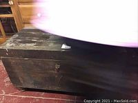 Solid wood chest showing wear and scuffs, rectangular shape with metal handles and feet, photographed from front and top angle.