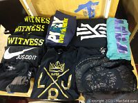 Nine men's shirts and one baseball cap assorted on a wooden surface showing graphic designs and brand logos for sale.