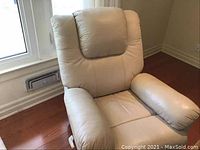 Front view of beige leather reclining chair showing cushioned headrest and padded armrest next to a window.