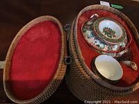 Wicker caddy opened showing porcelain teapot with lid and two cups inside, red fabric lining visible