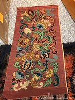 Full view of the needlepoint tapestry showing floral and scroll pattern on rust colored background