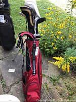 Two golf bags standing on patio; red Callaway bag with stand legs deployed in front
