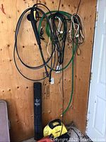 Yellow Karcher 320 pressure washer unit positioned on the floor with black hose attached and green and white hoses hanging on wooden wall.