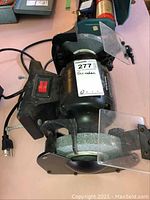 Photo showing the full bench grinder photo with power switch, grinding wheels, and attached safety shields.