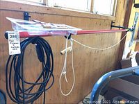 Corona red metal tree pruner with coiled black extension cord hanging on a wall