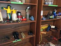 Multiple garden tools, sprayers, tape, and other hardware items organized on brown wooden shelves.