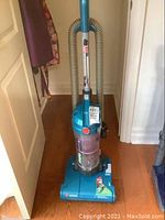 Full upright vacuum cleaner standing with hose attached on hardwood floor.