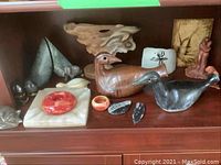Shelf display of various stone carved and pottery bird/statue items including ashtray, dishes and animal figures