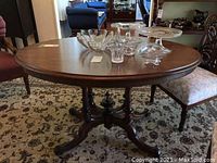 Full view of oval wood table showing wooden top surface and various glass items placed on it for scale.