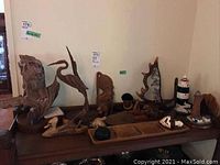 Wide view of table with various wood carved bird and animal sculptures plus bowls and lighthouses