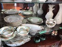 Shelf display of the lot containing Royal Crown Derby plates, Wedgwood bowls, Limoges dish and plates, and various vases including Irish and Belleek.