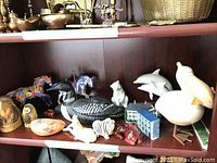 Shelf displaying a variety of animal figurines including painted ponies, loons, zebra, pottery buildings and a pelican.