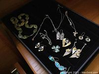 Full view of sterling silver jewelry pieces including earrings, pendants, rings, stone necklace, and trays all arranged in black velvet tray