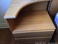 Close-up image showing the curved open shelf and three drawers of the end table with natural wood finish.