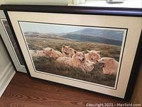 Photo showing complete framed print with artwork of wolves in wilderness landscape, matting and black frame visible.