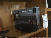 SkyCaddie SG5 rangefinder in original box with soft carrying case displayed on wooden shelf.