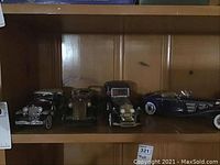 Shelf with four vintage-style metal diecast car replicas in silver, brass, black and navy finishes