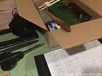 Overview of box containing rulers, brush, pencils, erasers, electric pencil sharpener, and drafting tools on table.