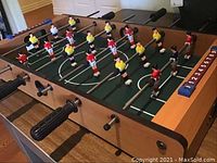 Front-side overview of the entire foosball table showing playing surface, rods, players, and score counters