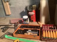 Overview of the woodworking tools including extractor cutting tool set in an orange case, Millers Falls chisels to the right, paint brushes in a coffee tin, and a roll of paper towels.