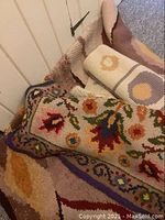 Photo showing three stacked hooked rugs with floral and geometric designs, rolled and layered, detailing colors and texture.