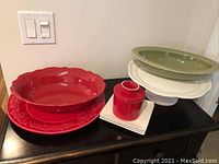 Photo showing red serving bowl with embossed floral rim, red butter keeper on white base, cream serving platter, green serving bowl, and cake stand.