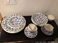 Photo of full dinnerware set displaying all plates, bowls, saucers, and tea cups arranged on a dark surface.