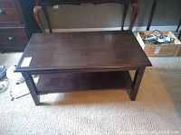 Full view of the wood coffee table showing the top and bottom shelf on carpeted floor.