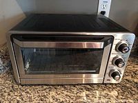Front view of stainless steel Cuisinart toaster oven featuring glass door and three control knobs on the right side.