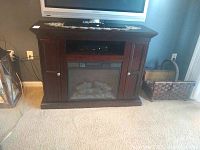 Full frontal view of dark wood electric fireplace cabinet with TV on top, showing the fireplace insert, side doors with storage, and remote on top.