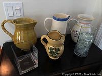 Wide shot showing all four ceramic pitchers and two glass flower holders on black table.