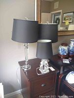 Photo showing the three lamps with crystal or glass bases and black lampshades on two wooden tables.
