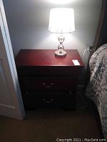 Nightstand with lamp atop, showing whole piece in situ next to bed and closet door.