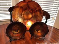 Three glass decorative plates on stands shown on a wooden table with light from window highlighting amber and brown swirling glass patterns.