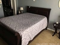 Full view of queen mahogany wood sleigh bed with patterned bedding and pillow top mattress on carpeted floor.