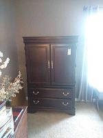 Front full view of the dark wooden television cabinet against a wall, showing its two doors and two drawers with metal handles.